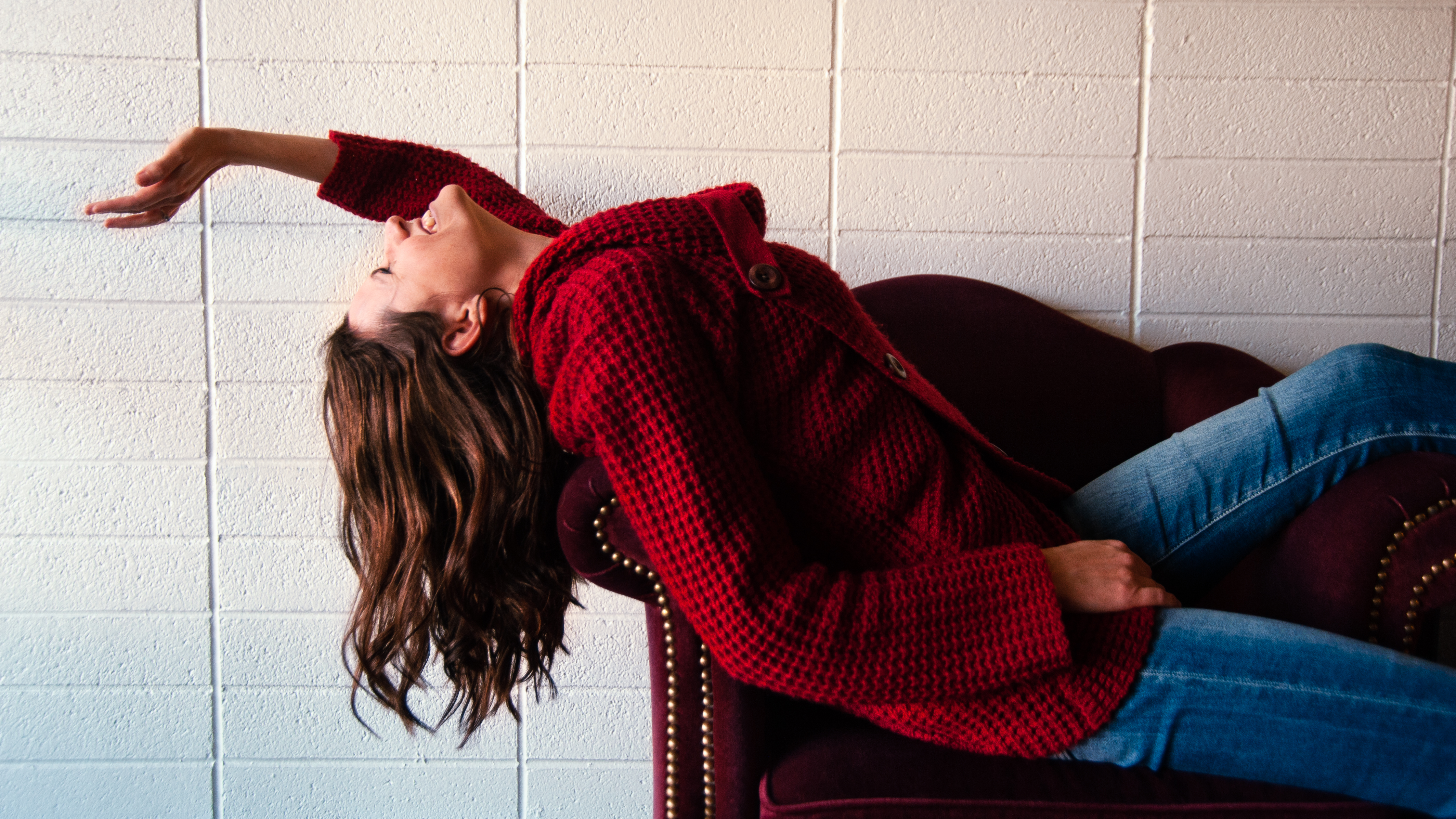 Diana lays down dramatically on couch in red sweater